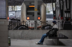 ep un hombre protegido con una mascarilla espera sentado en un banco en una estacion de tren de