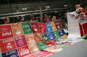 ep el personaje sustainaclaus junto a un cartel de los objetivos de desarrollo sostenible ods de la