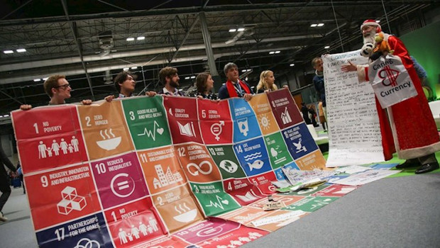 ep el personaje sustainaclaus junto a un cartel de los objetivos de desarrollo sostenible ods de la